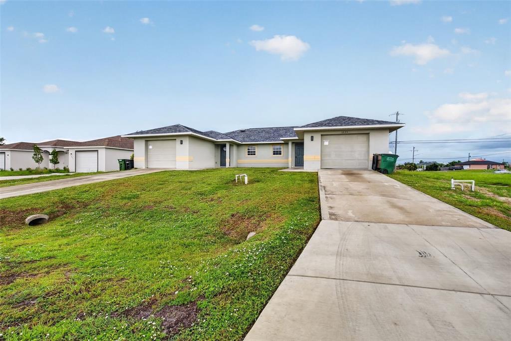 A duplex with two garages and concrete driveways sits on a grassy lot under a sky — 1223/1225 NE 15TH LANE, CAPE CORAL, FL