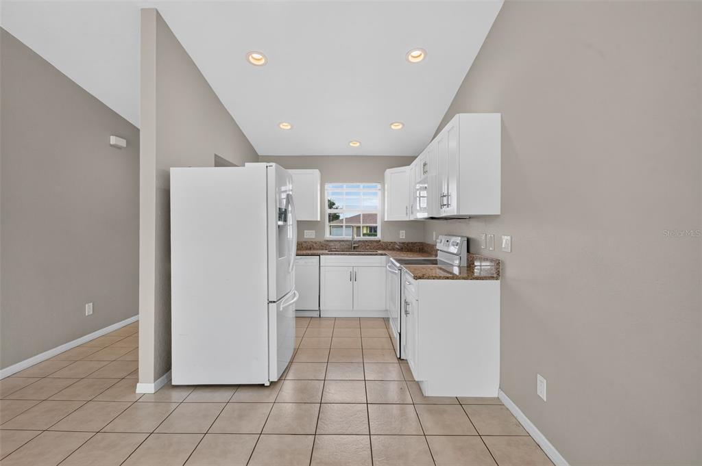A kitchen features white cabinets, granite countertops, a white refrigerator, and light-colored tile flooring — 1223/1225 NE 15TH LANE, CAPE CORAL, FL