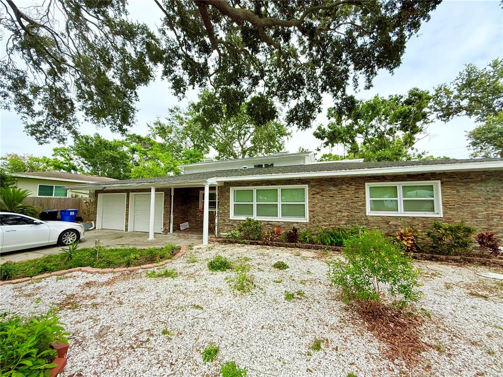 A single-story house with a stone facade, white garage doors, and a white gravel front yard — 1557 ROBINSON DRIVE N, ST PETERSBURG, FL