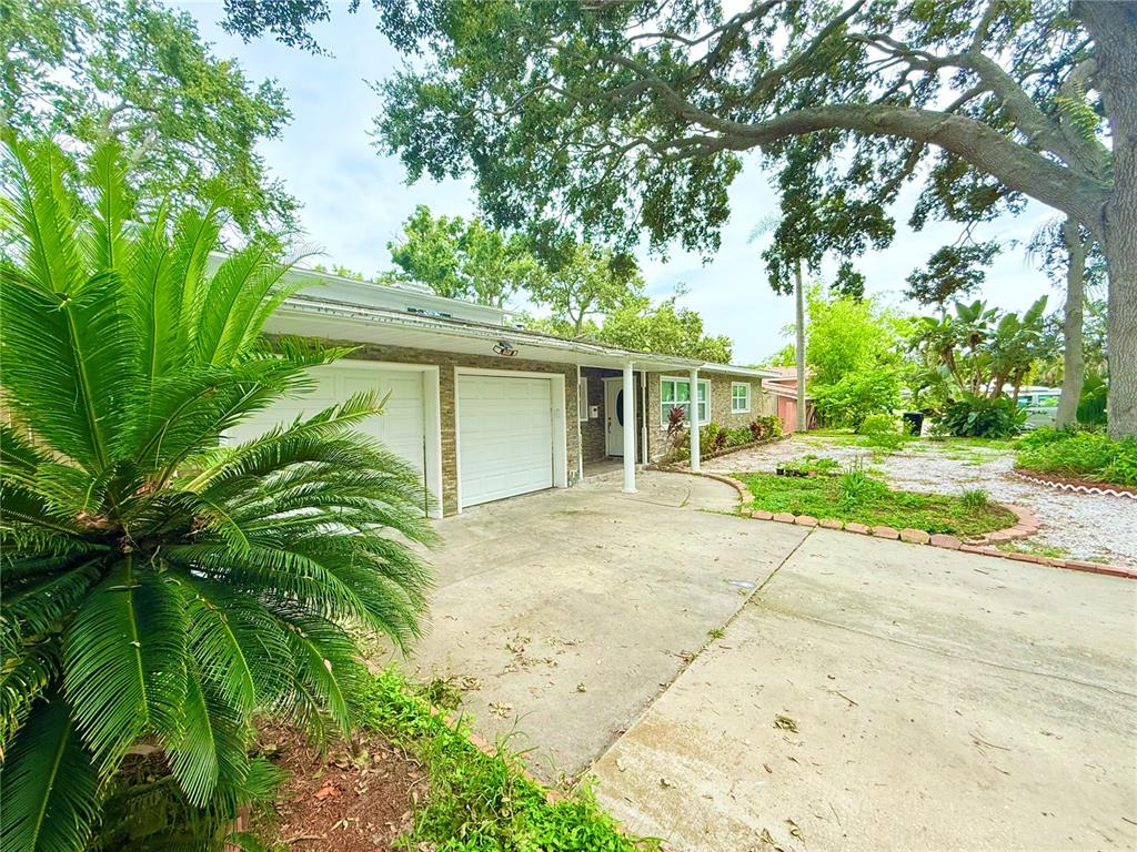 A single-story house with a two-car garage, concrete driveway, and large trees in the yard — 1557 ROBINSON DRIVE N, ST PETERSBURG, FL