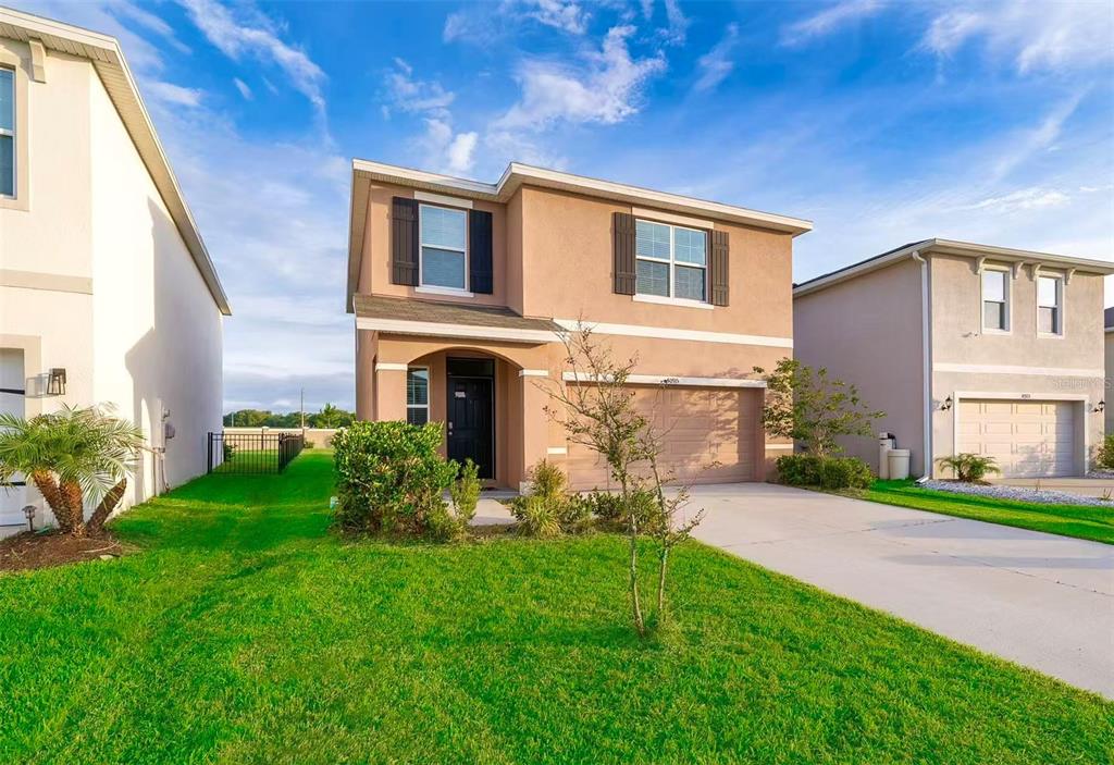 A two-story tan stucco house with a two-car garage and a front lawn — 30915 PENNY SURF LOOP, WESLEY CHAPEL, FL