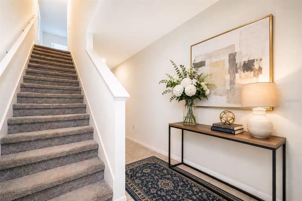 A staircase with gray carpet sits beside a console table, artwork, and a patterned rug — 30915 PENNY SURF LOOP, WESLEY CHAPEL, FL