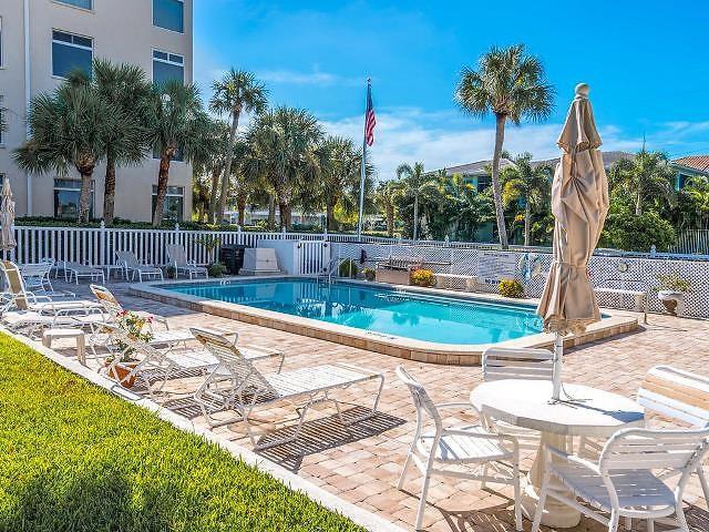 A swimming pool with lounge chairs and a patio area sits beside a multi-story building — 716 GRANADA AVENUE UNIT 302, VENICE, FL