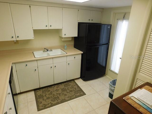 A kitchen features white cabinets, a black refrigerator, a double sink, and tiled flooring — 716 GRANADA AVENUE UNIT 302, VENICE, FL