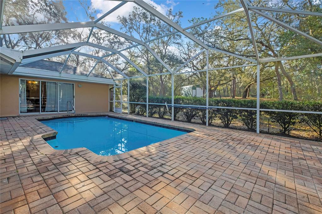 A screened-in pool patio features brick pavers and a view of trees and a shed — 340 E SAVOY STREET, LECANTO, FL