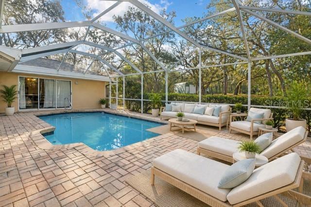 A swimming pool with a screened enclosure sits on a brick patio near lounge chairs — 340 E SAVOY STREET, LECANTO, FL