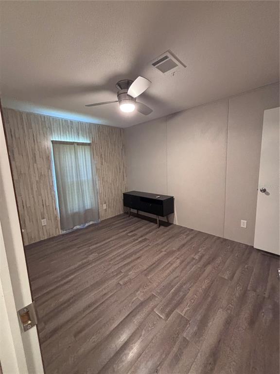 An empty bedroom features wood-look flooring, a ceiling fan, and a wood-paneled accent wall — 133 OAK CIRCLE, INTERLACHEN, FL