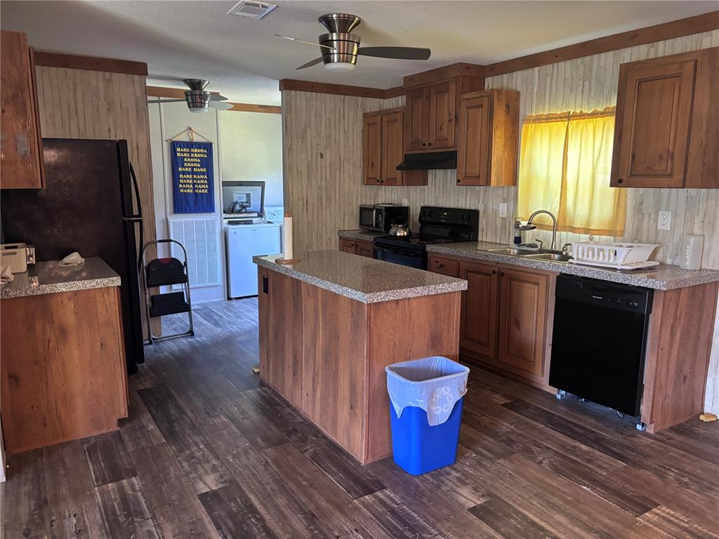A kitchen with wood-look cabinets, granite countertops, black appliances, and wood-patterned flooring — 133 OAK CIRCLE, INTERLACHEN, FL
