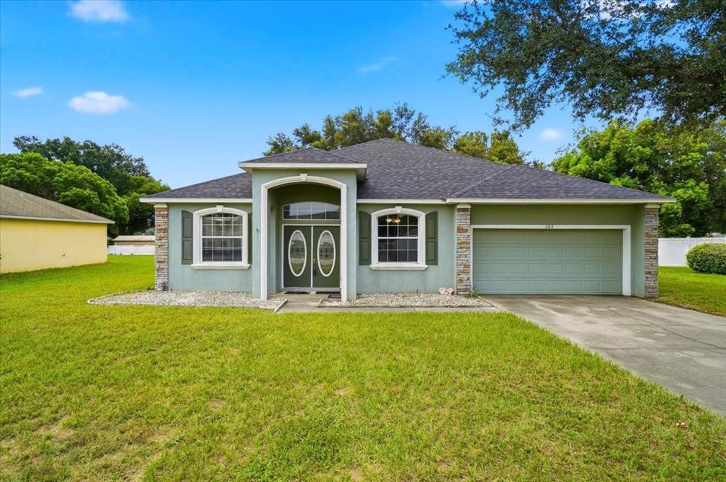 A single-story house with a green stucco exterior, a two-car garage, and a front entryway — 153 OAK CROSSING BOULEVARD, AUBURNDALE, FL