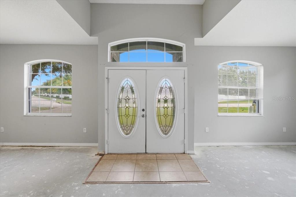An entryway with double glass-paneled doors, arched windows, and unfinished concrete flooring — 153 OAK CROSSING BOULEVARD, AUBURNDALE, FL