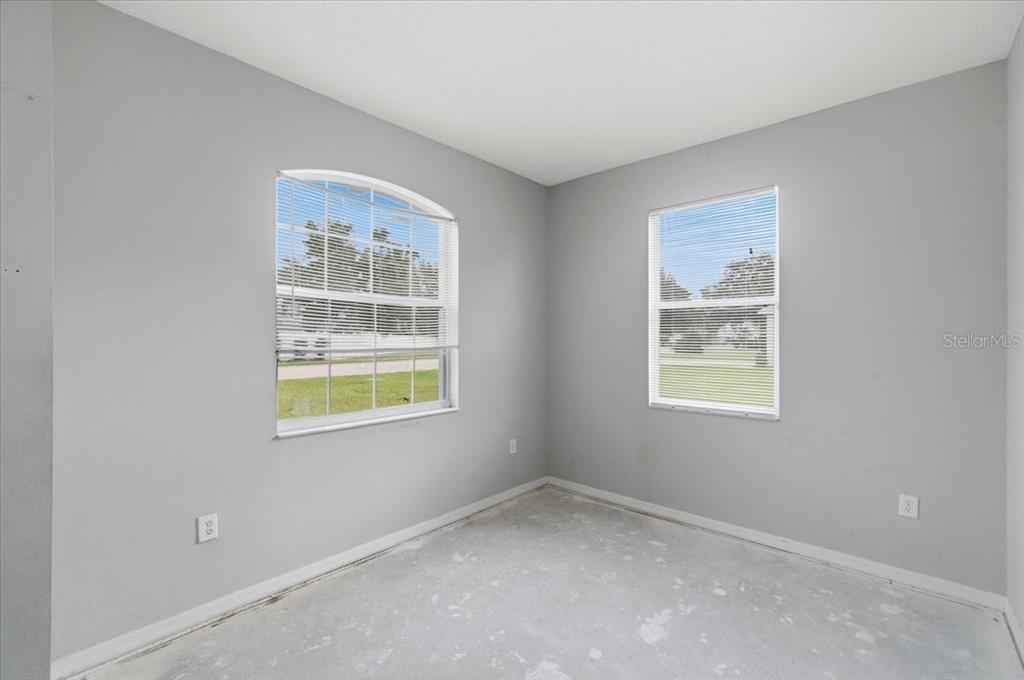 An empty room with gray walls, two windows, and an unfinished concrete floor — 153 OAK CROSSING BOULEVARD, AUBURNDALE, FL