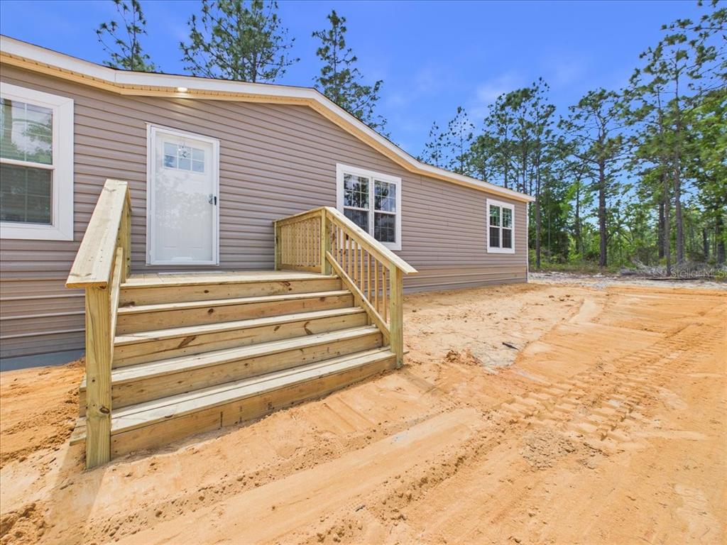 A single-story manufactured home with tan siding sits on a cleared, sandy lot — 137 BEULAH DRIVE, HAWTHORNE, FL