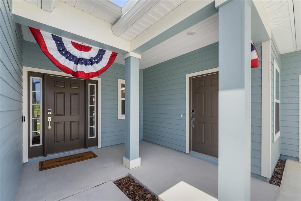 A covered front porch with blue siding, two brown doors, and patriotic bunting — 13941 NW CONVERGENCE BOULEVARD, ALACHUA, FL
