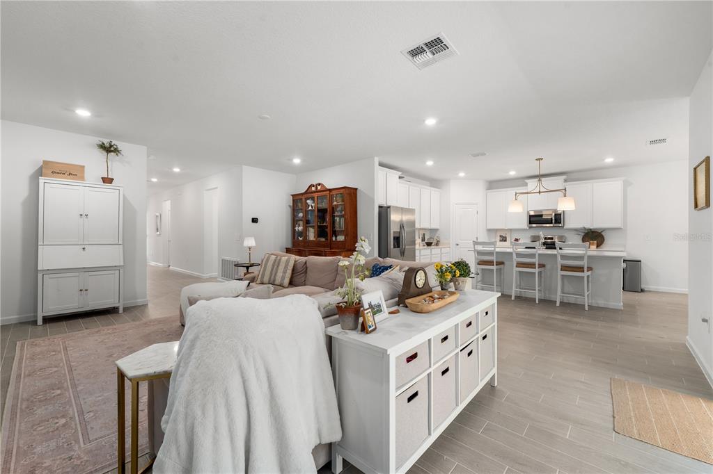 A bright open-concept living room and kitchen featuring light tile flooring and white cabinetry — 13941 NW CONVERGENCE BOULEVARD, ALACHUA, FL