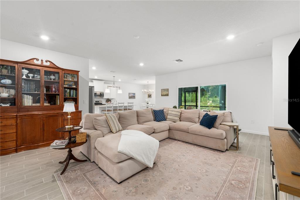 A white kitchen features a central island with three chairs and a dining area nearby — 13941 NW CONVERGENCE BOULEVARD, ALACHUA, FL
