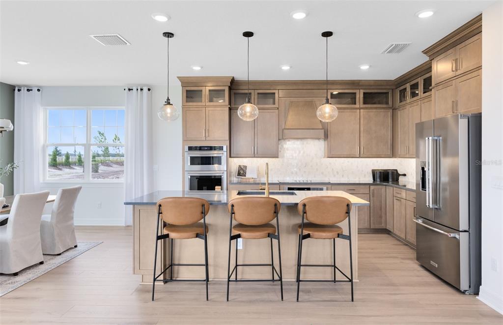 A modern kitchen features light wood cabinets, a central island with barstools, and stainless appliances — 1538 VALIER POINT, ZEPHYRHILLS, FL