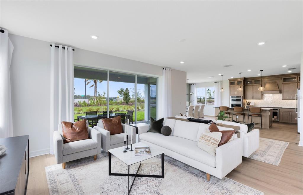 A bright living room with a white sofa, two armchairs, and an open-concept kitchen beyond — 1538 VALIER POINT, ZEPHYRHILLS, FL