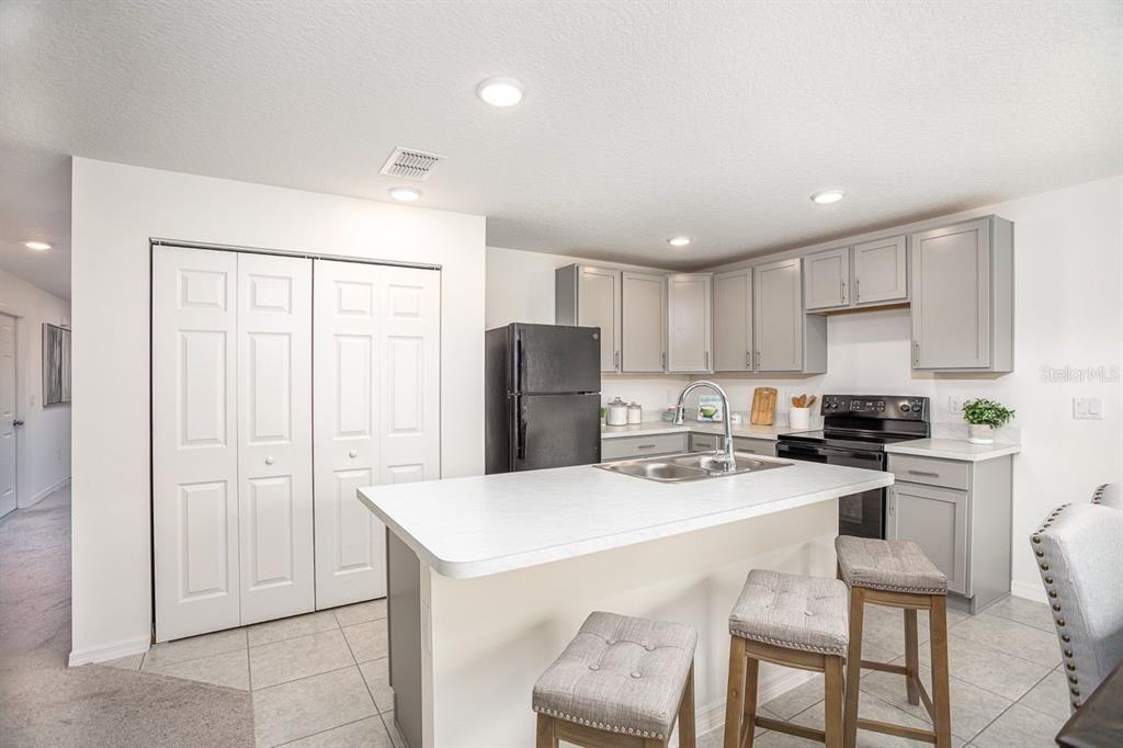A kitchen features gray cabinets, a white island with bar stools, and black appliances — 3104 MANDRELL AVENUE, SPRING HILL, FL