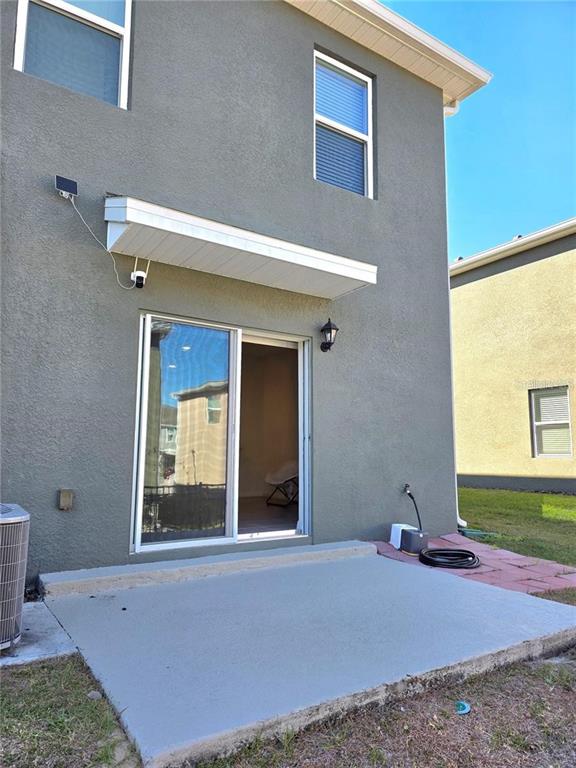A gray stucco house exterior features a concrete patio, sliding glass door, and security camera — 2333 PENGUIN BOULEVARD, DAVENPORT, FL