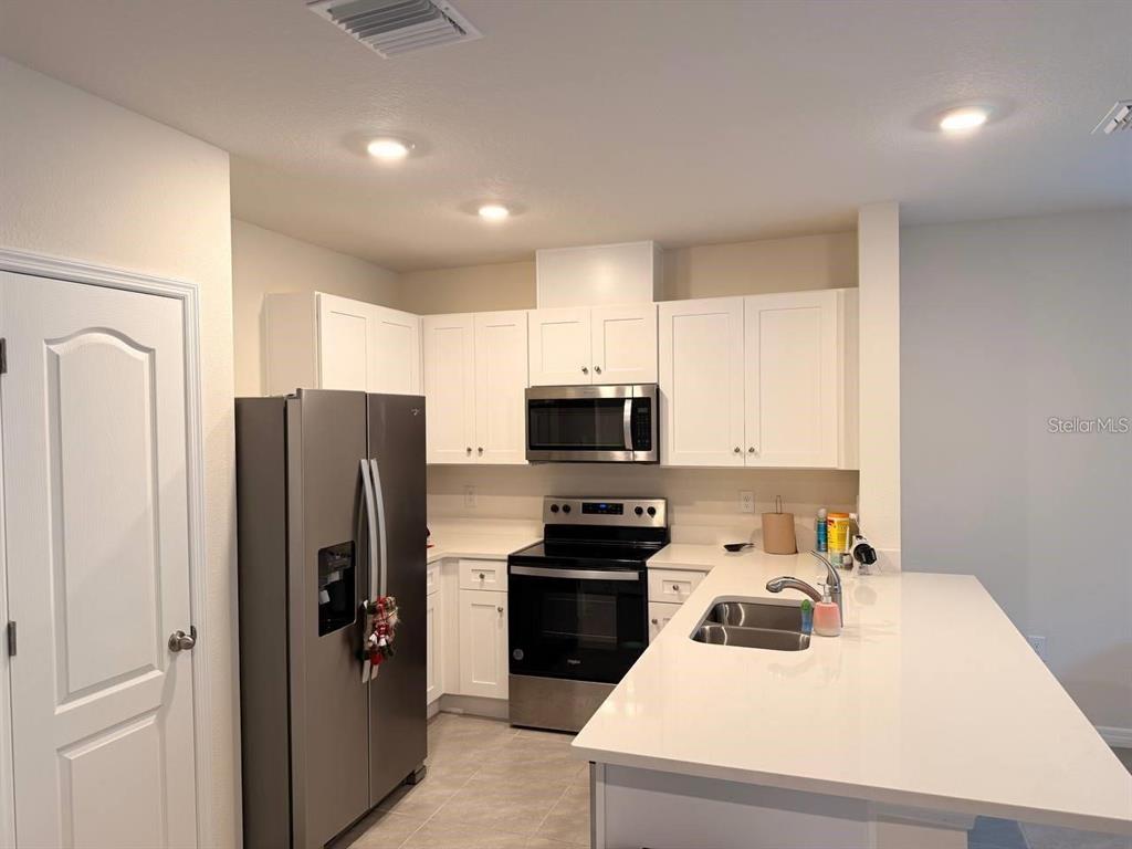 A kitchen features white cabinets, stainless steel appliances, and a large white quartz island — 2333 PENGUIN BOULEVARD, DAVENPORT, FL
