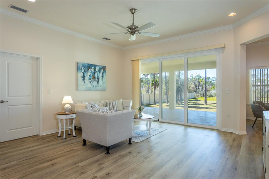 A living room features light wood-look flooring, a ceiling fan, and sliding glass patio doors — 1591 LAMBERT AVENUE, FLAGLER BEACH, FL