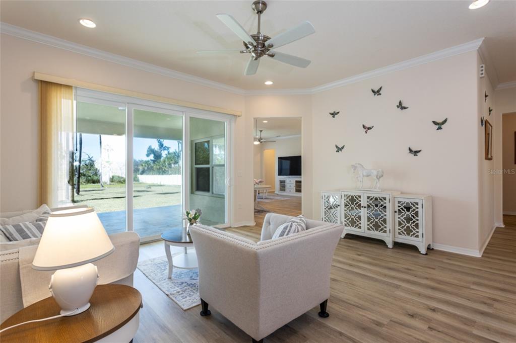 A living room features light-colored furniture, wood-look flooring, a ceiling fan, and sliding glass doors — 1591 LAMBERT AVENUE, FLAGLER BEACH, FL
