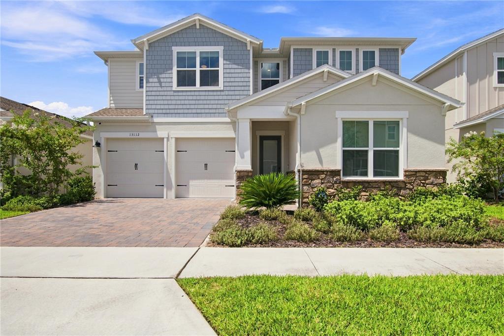 A two-story suburban house features a two-car garage, stone accents, and light-colored siding — 13112 DENDY WAY, WINTER GARDEN, FL