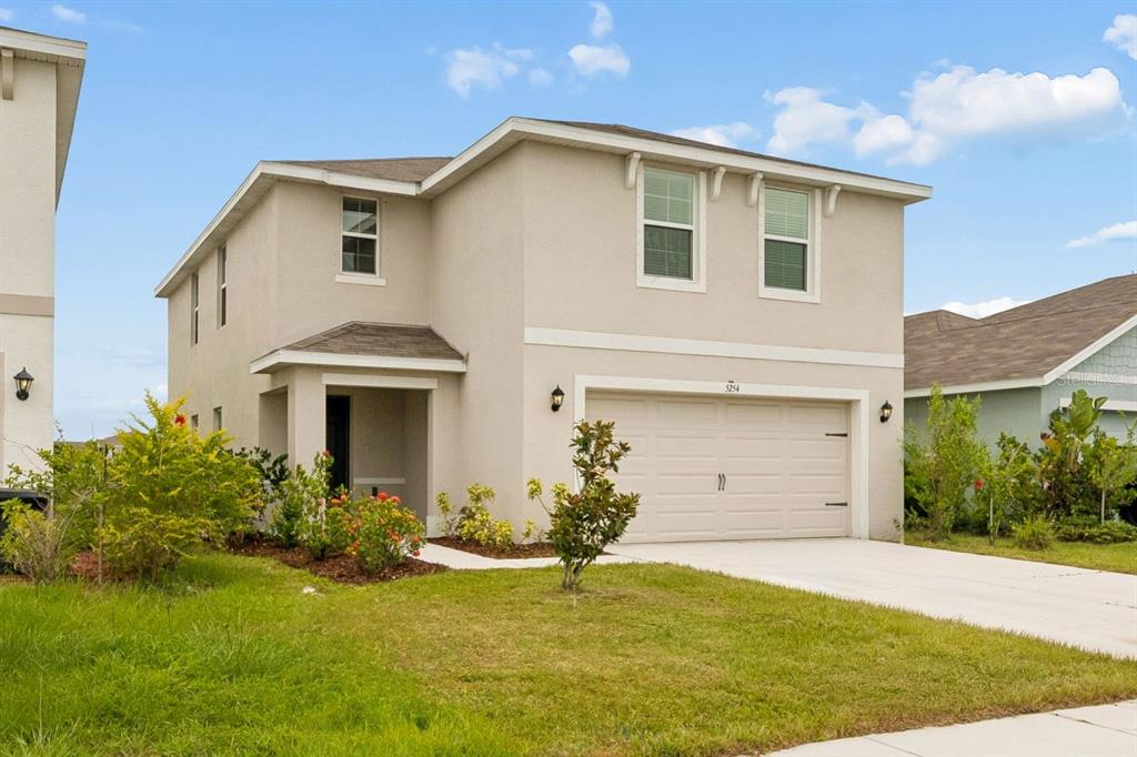 A two-story suburban house features a two-car garage, light-colored stucco siding, and a concrete driveway — 5254 ROCKY COAST PLACE, PALMETTO, FL