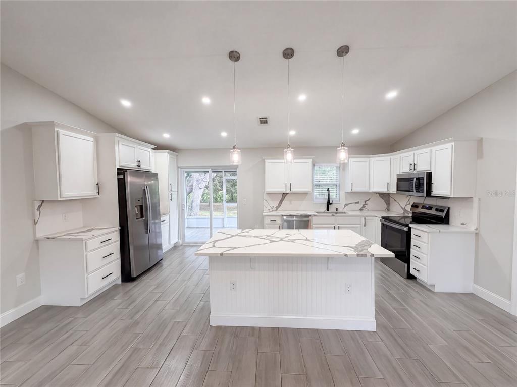 A modern kitchen features white cabinetry, a marble-topped island, stainless steel appliances, and wood-look flooring — 8165 RIDGE ROAD, WEEKI WACHEE, FL