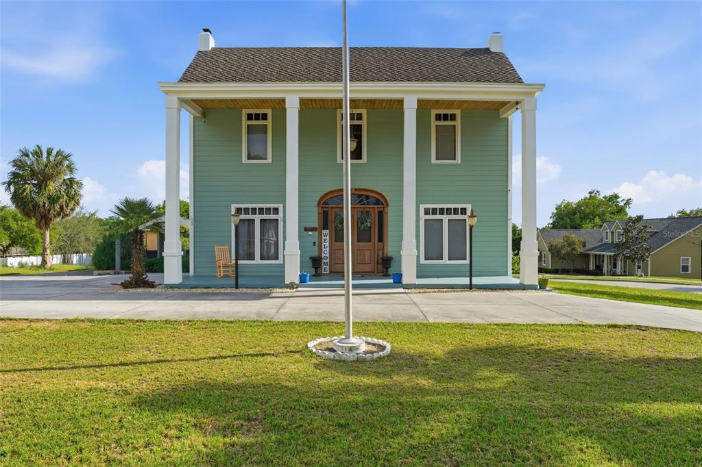 A two-story green house with a front porch, white columns, and a flagpole — 835 BUTCH CASSIDY LANE, EUSTIS, FL