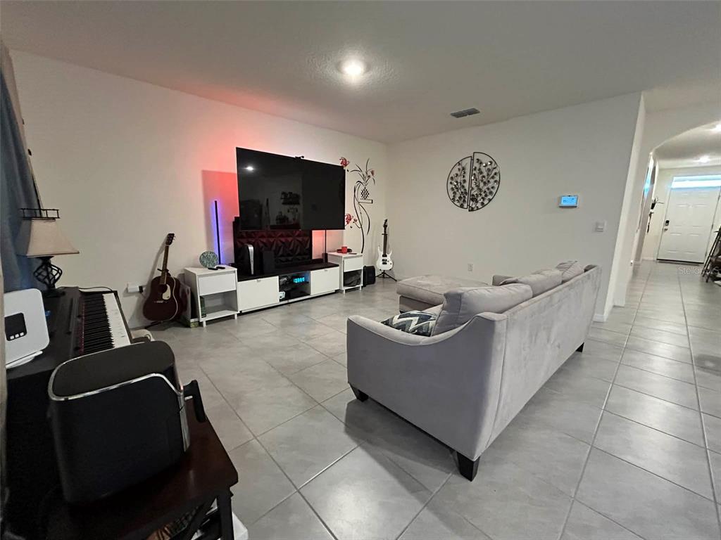 A living room features a large television, a gray sofa, and tile flooring — 2612 HARMONIA HAMMOCK ROAD, HARMONY, FL