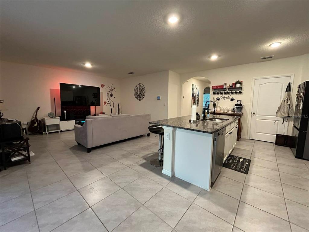 An open-concept living room and kitchen featuring tile flooring, a kitchen island, and a television — 2612 HARMONIA HAMMOCK ROAD, HARMONY, FL