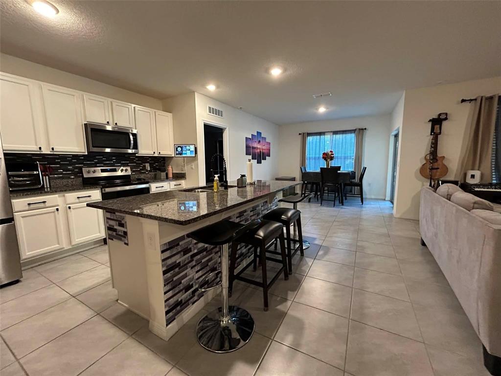 A kitchen with white cabinets, a granite island, and bar stools opens to a dining area — 2612 HARMONIA HAMMOCK ROAD, HARMONY, FL