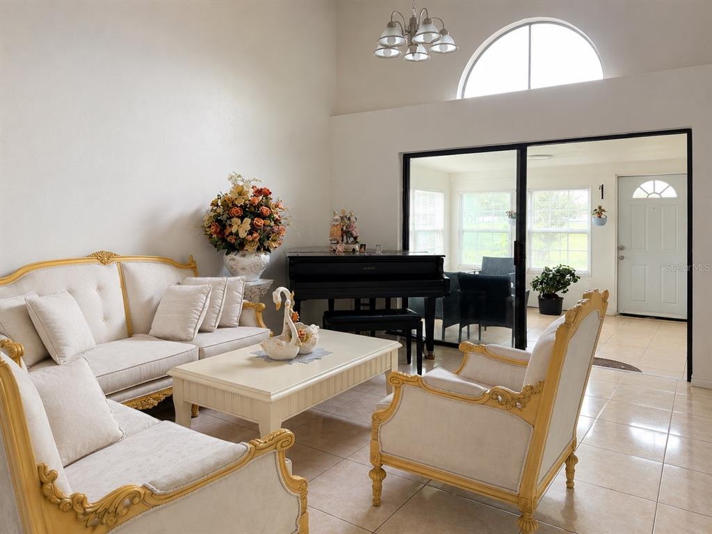 A living room features a grand piano, ornate furniture, and a sliding door to a sunroom — 499 CHICAGO WOODS CIRCLE, ORLANDO, FL