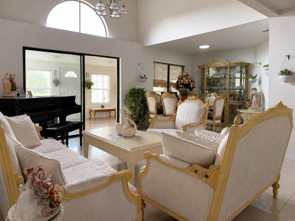 A living room features ornate cream-colored furniture, a black piano, and a large arched window — 499 CHICAGO WOODS CIRCLE, ORLANDO, FL