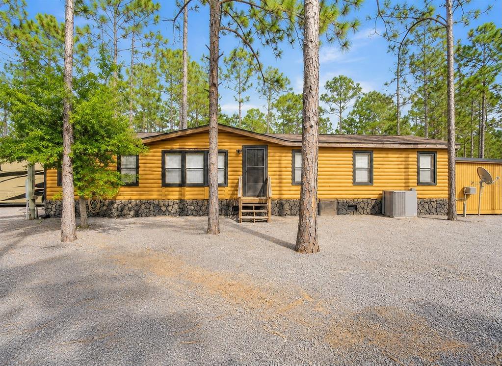 A yellow log-style manufactured home sits on a gravel lot surrounded by pine trees — 5660 E 630 HIGHWAY, FROSTPROOF, FL