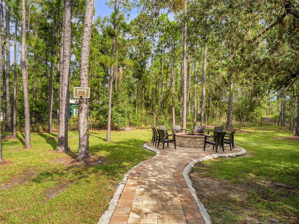 A stone fire pit with chairs sits at the end of a paved walkway outdoors — 5660 E 630 HIGHWAY, FROSTPROOF, FL