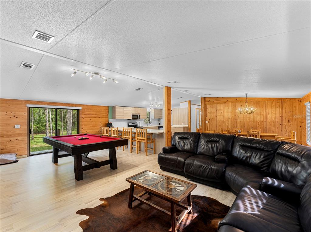 A living room with a pool table, leather sectional, and wood-paneled walls opens to a kitchen — 5660 E 630 HIGHWAY, FROSTPROOF, FL