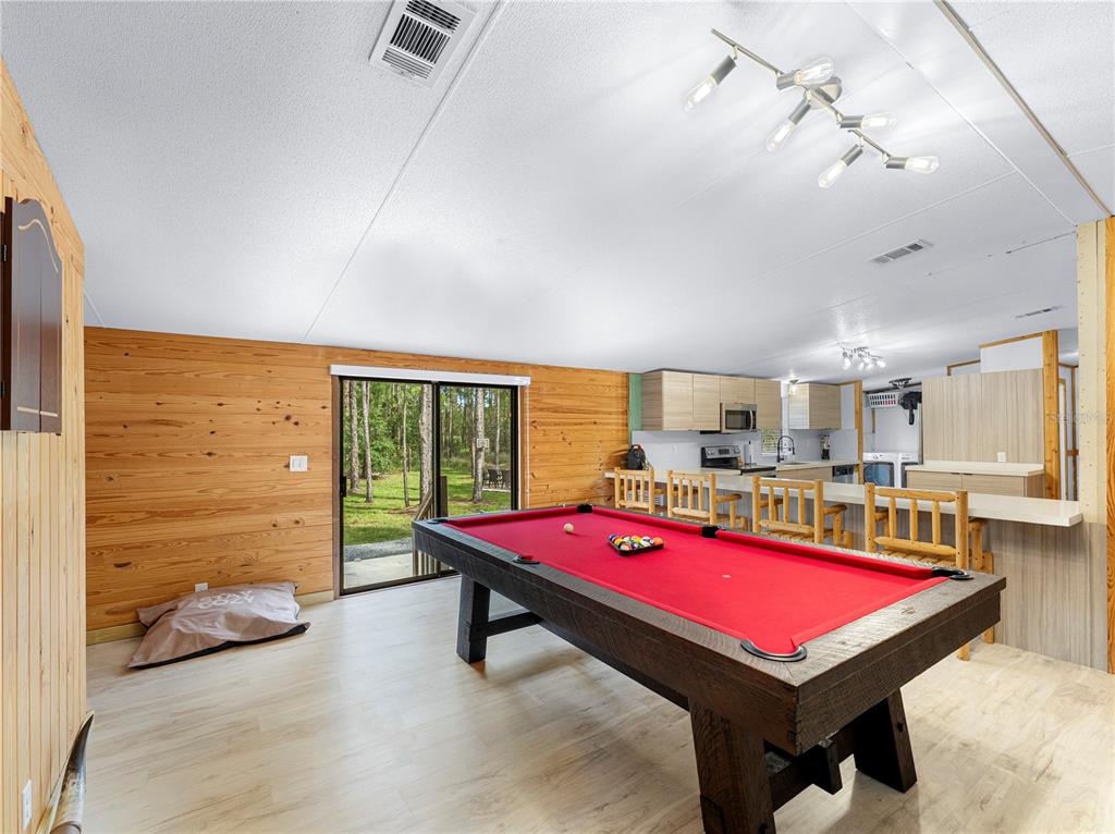 A game room with a red pool table, wood-paneled walls, and an open kitchen area — 5660 E 630 HIGHWAY, FROSTPROOF, FL