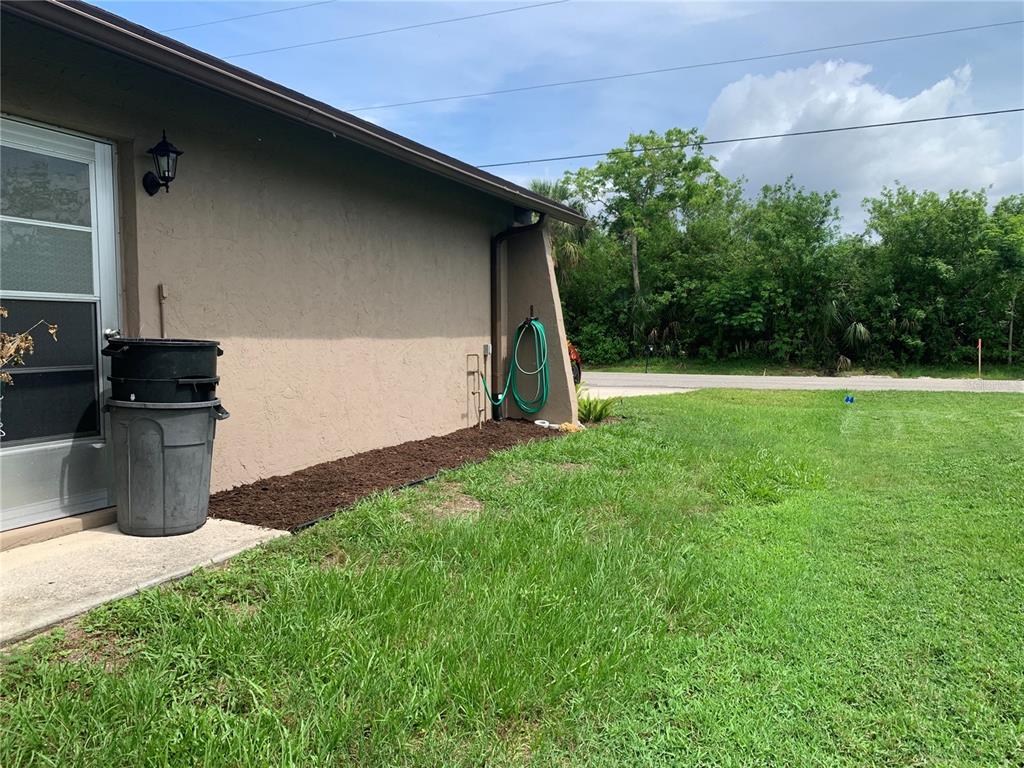 The exterior of a house features a tan stucco wall, a mulch bed, and a lawn — 18094 ACKERMAN AVENUE, PORT CHARLOTTE, FL