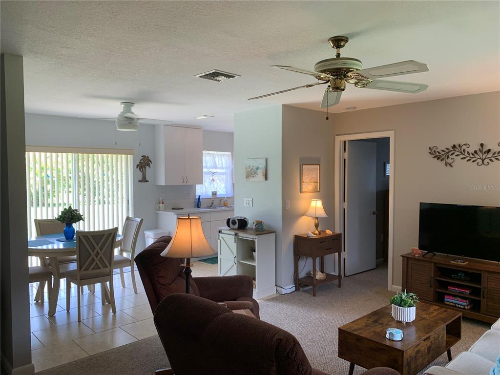 A living room with carpeted floors flows into a tiled dining area and kitchen — 18094 ACKERMAN AVENUE, PORT CHARLOTTE, FL