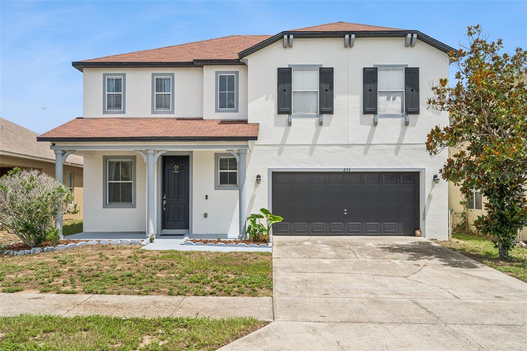 A two-story house with a covered front porch, a garage, and a small front yard — 233 ROSSELLI BOULEVARD, DAVENPORT, FL