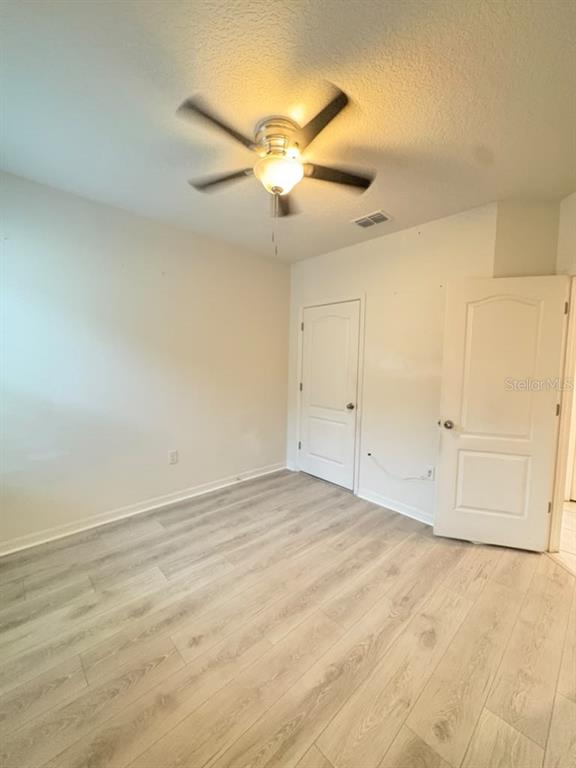 A bedroom features a tufted headboard, light wood-look flooring, and a ceiling fan — 329 WINGED ELM DRIVE, DEBARY, FL