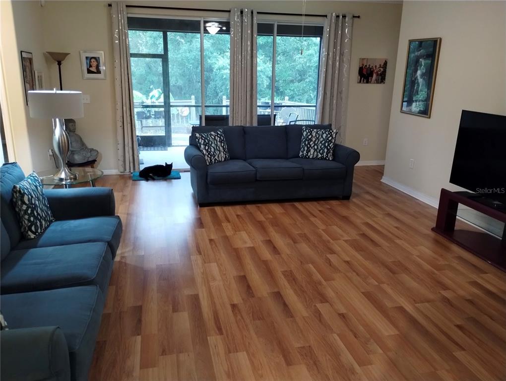 A living room features blue sofas, wood-look flooring, and sliding glass doors leading to a deck — 12722 DRAKEFIELD DRIVE, SPRING HILL, FL