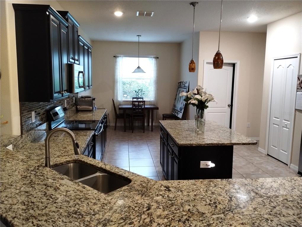 A kitchen with dark cabinets, granite countertops, a center island, and an adjacent dining area — 12722 DRAKEFIELD DRIVE, SPRING HILL, FL