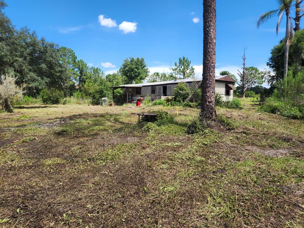 A weathered mobile home sits on a large, cleared lot with scattered trees and vegetation — 7244 GROVELAND FARMS ROAD, GROVELAND, FL