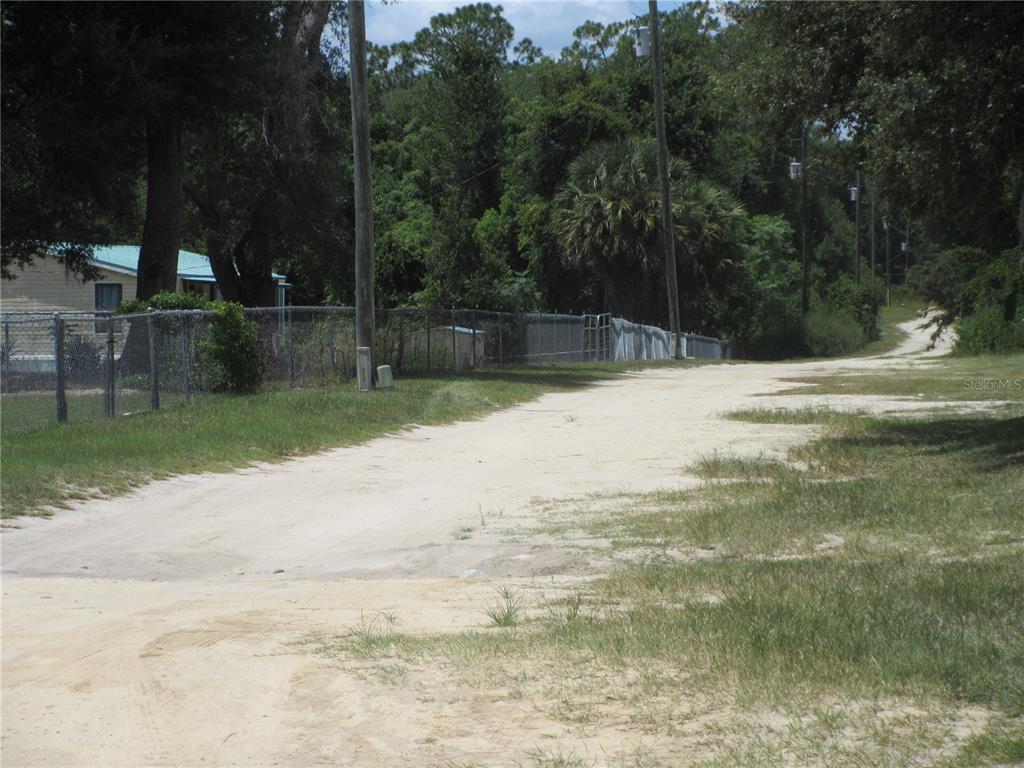 A dirt road leads past a chain-link fence and a house toward a wooded area — TBD SE 18TH STREET, SILVER SPRINGS, FL