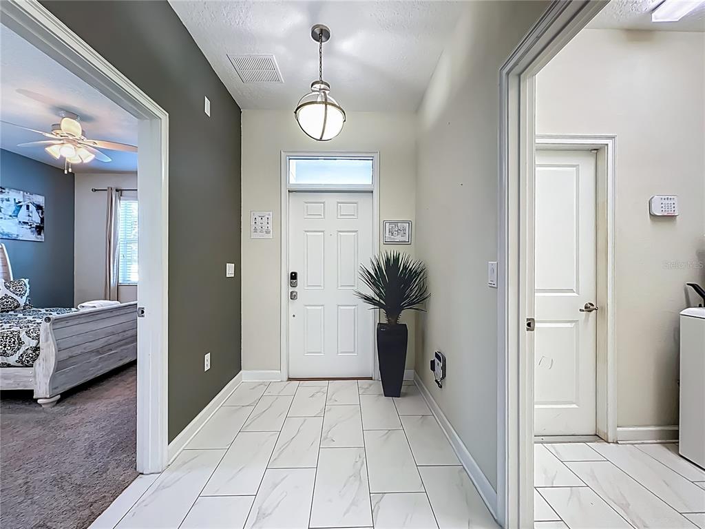 A bright entryway features white tile flooring, a central pendant light, and a white front door — 9018 STINGER DRIVE, DAVENPORT, FL