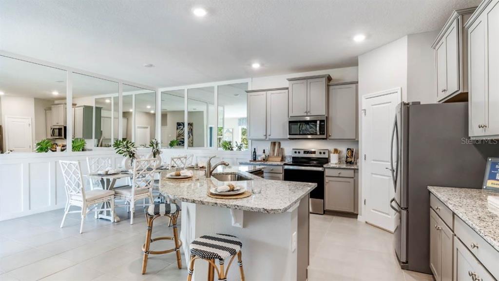 A kitchen with gray cabinets, granite countertops, and a breakfast bar next to a dining area — 316 157TH COURT E, BRADENTON, FL