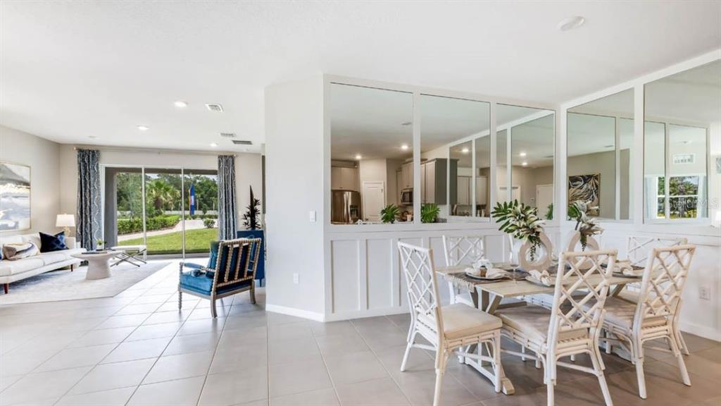 A dining area with white lattice chairs sits beside a living room with glass doors — 316 157TH COURT E, BRADENTON, FL